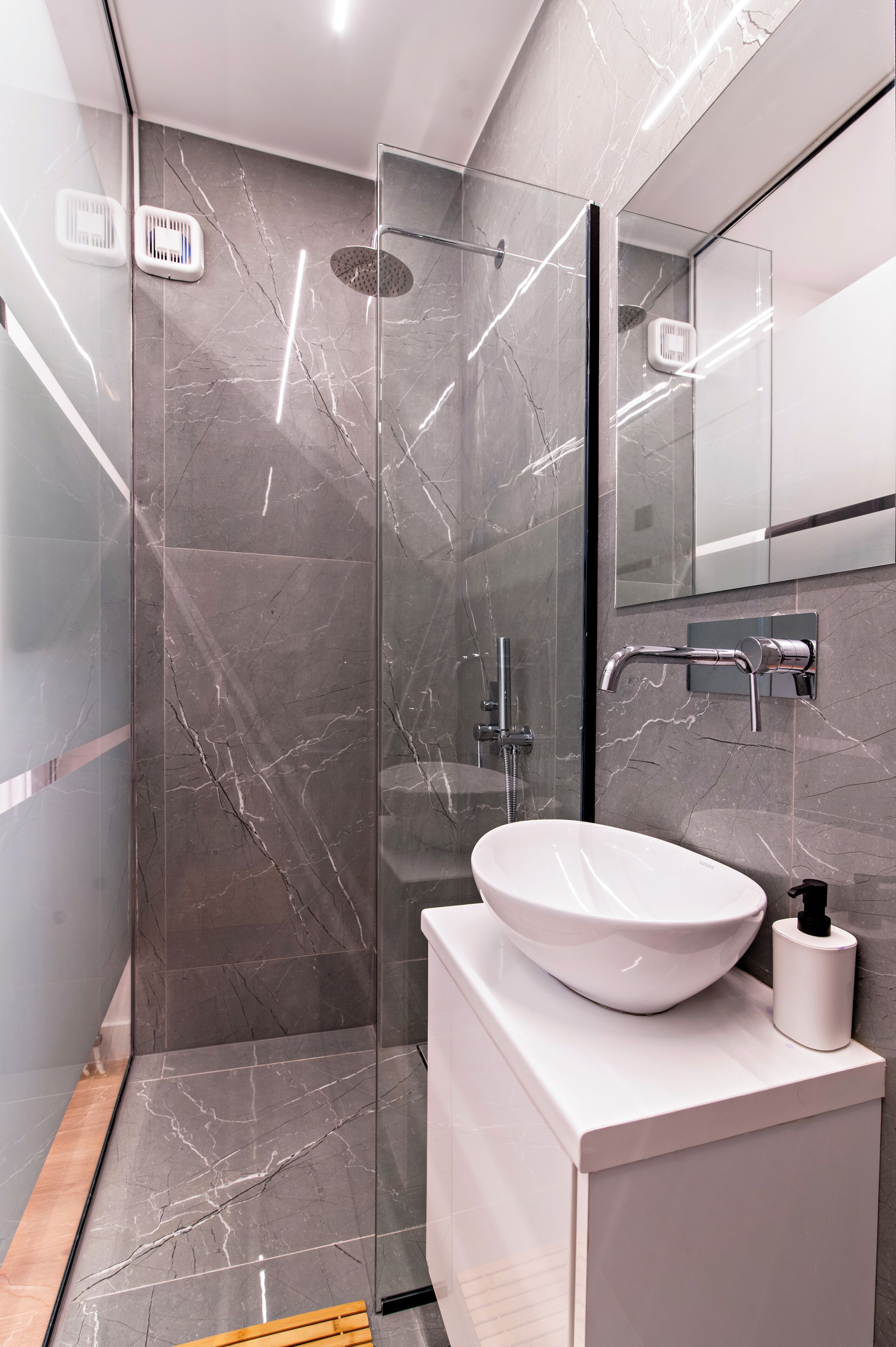 Een moderne badkamer met een douchecabine van glas, een witte wastafel en een vloer van marmer.