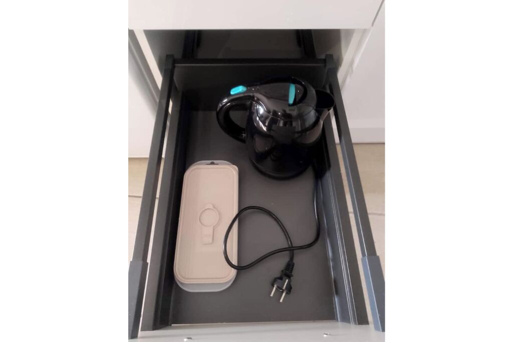 A drawer containing a black kettle, a beige phone, and a black charging cable.