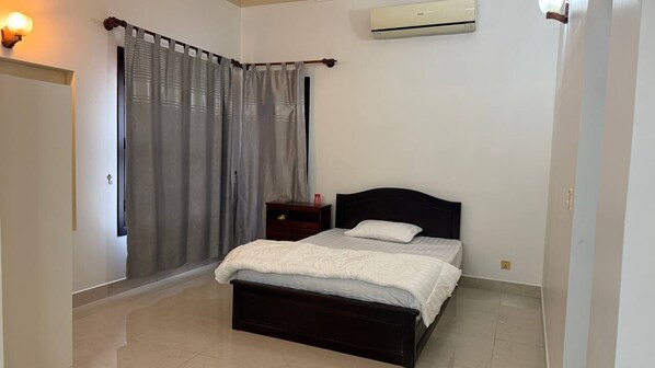 A bedroom with a bed, a nightstand, a wall-mounted air conditioner, and a window with curtains.