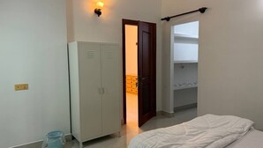 Een slaapkamer met een bed, een kledingkast, een deur naar een badkamer en een wandplank.
