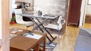 Ett modernt vardagsrum med ett matbord i glas, vita stolar, ett soffbord i trä och en stor accentvägg i sten.