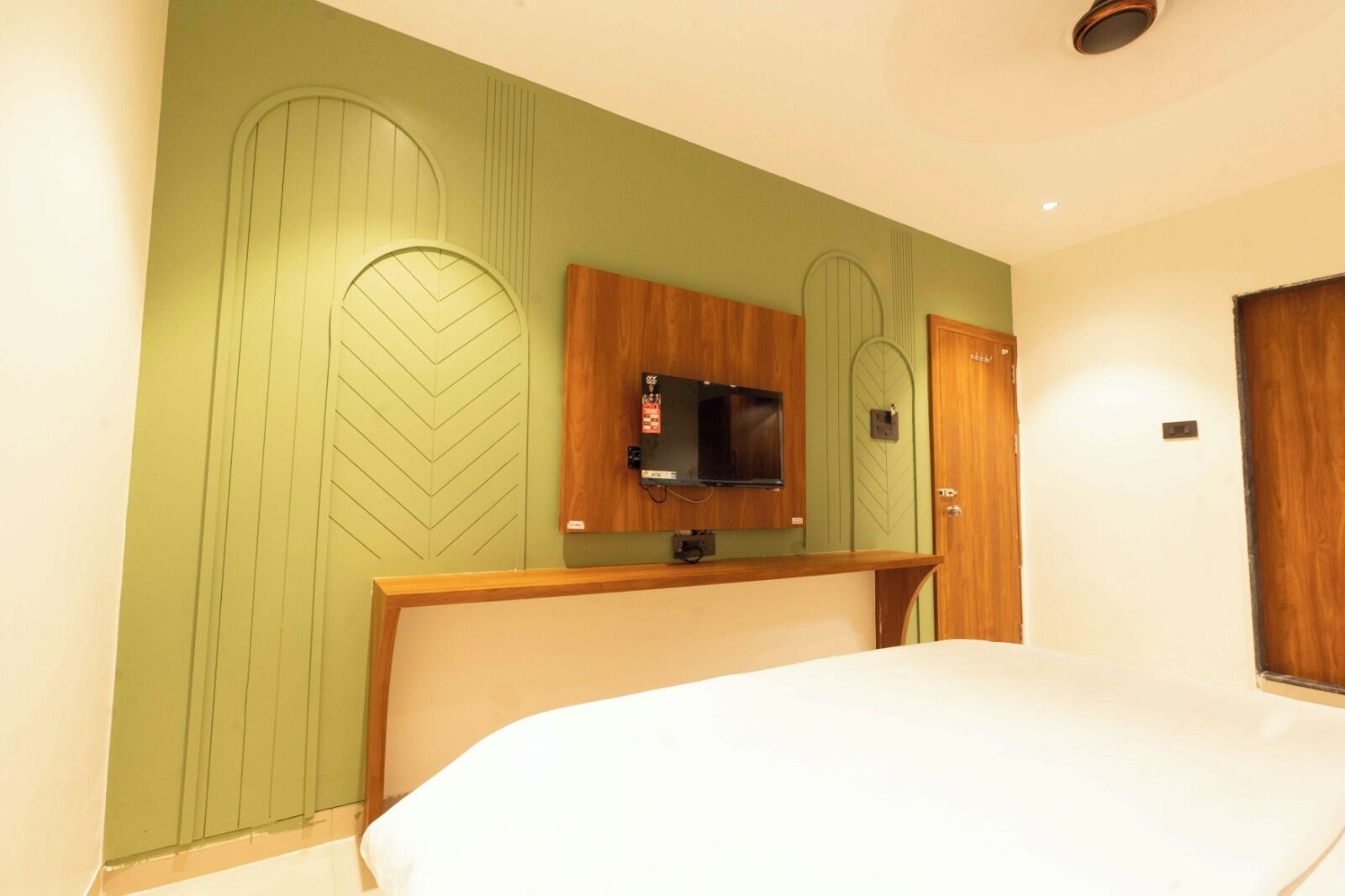 Una habitación de hotel con una cama, un televisor montado en la pared y una puerta de madera.