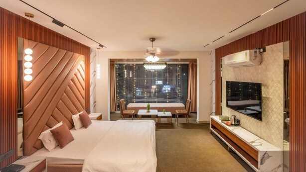 A modern hotel room with a large bed, a seating area, a TV, and a city view. - Majestic Inn (Pune)