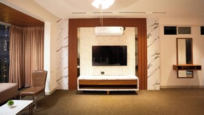 A modern hotel room with a large TV mounted on a marble wall, a wooden vanity, and a ceiling fan. - Majestic Inn (Pune)
