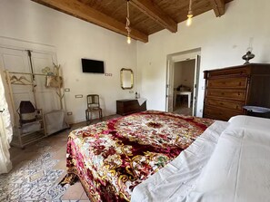 A bedroom with a large bed, a wooden dresser, a chair, a mirror, and a hanging light fixture. - Grandpa Michele's House, Minori - Amalfi Coast- A Paradise in the countryside (Campania)