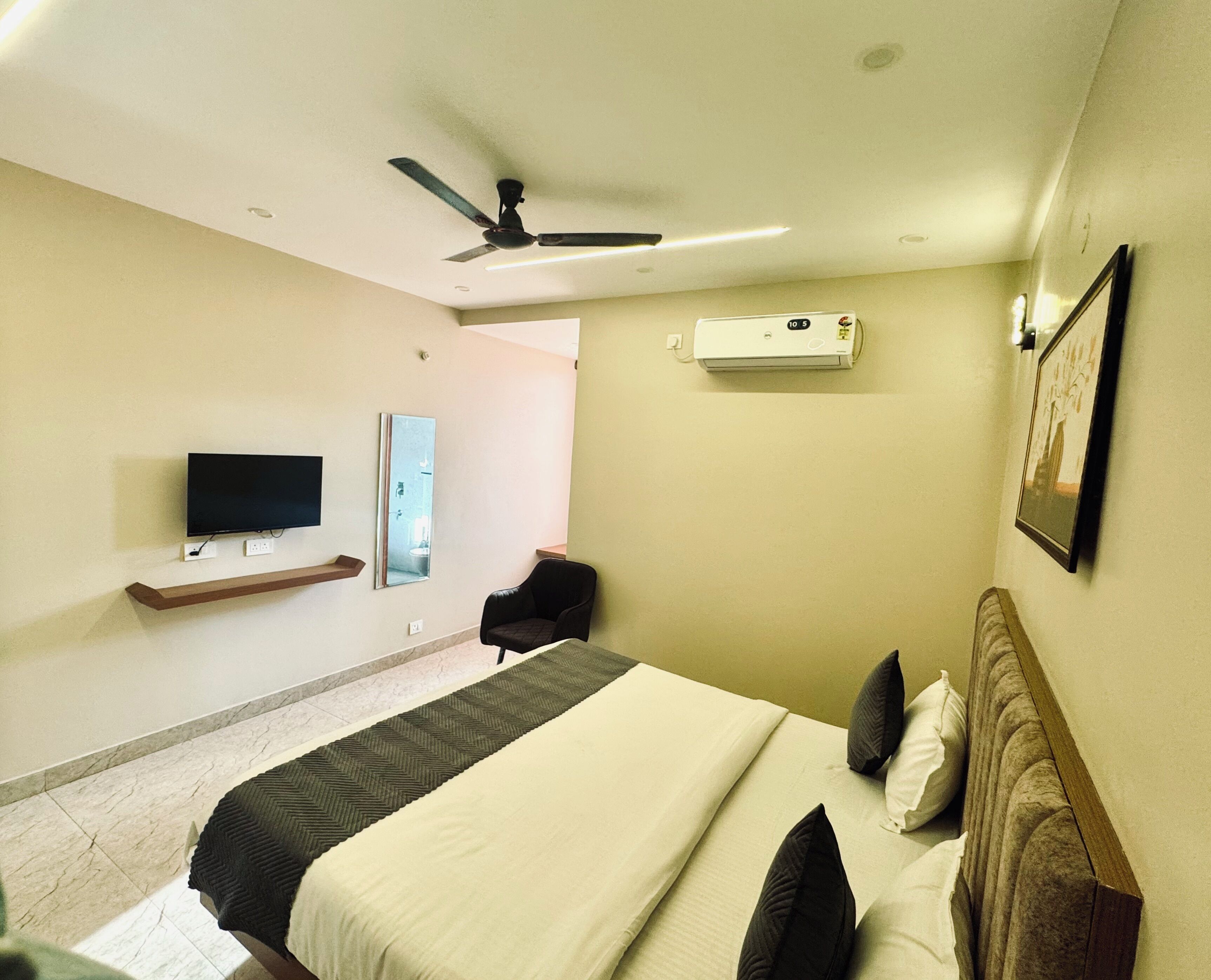 A hotel room with a bed, a television, a ceiling fan, an air conditioning unit, a chair, and a framed picture on the wall.