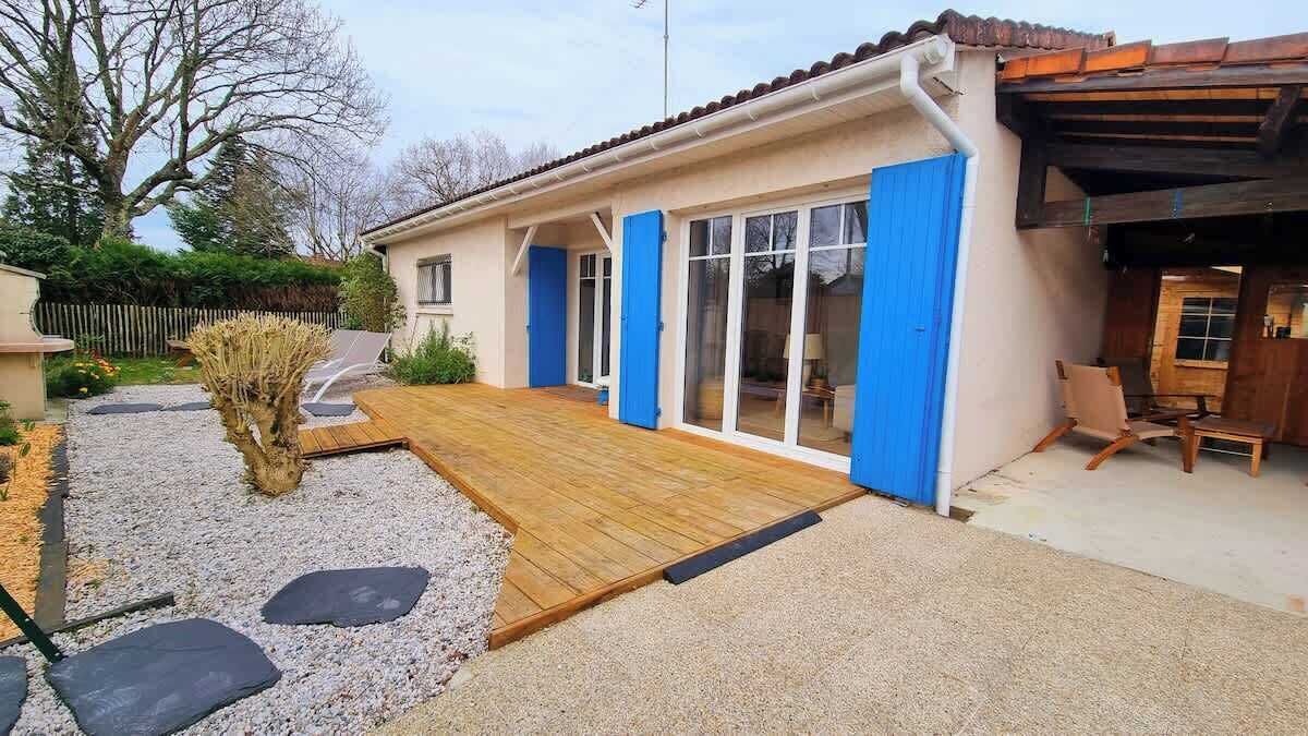 A house with a wooden deck, a covered patio, and a garden with stepping stones.