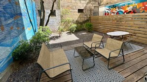 Une terrasse extérieure avec une table et des chaises, entourée d’un mur de pierre orné d’une fresque colorée.