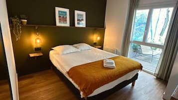 Habitación de hotel con cama, dos lámparas de noche, ventana con cortinas y vistas al exterior.