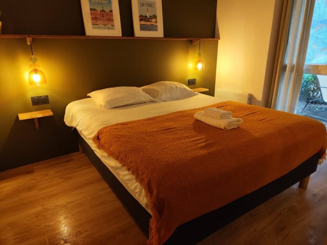 A neatly made bed with a white comforter and a brown blanket, two bedside lamps, and a small wooden nightstand with a lamp.