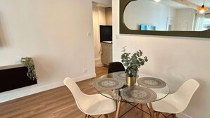 Un coin repas avec une table ronde, quatre chaises, une plante en pot et un grand miroir au mur.