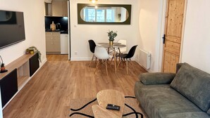 Ein modernes Wohnzimmer mit einer Couch, einem Fernseher und einem Essbereich mit Tisch und Stühlen.