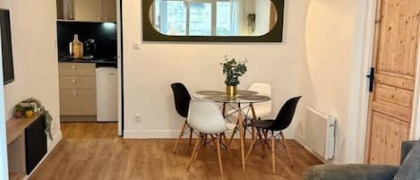A compact living space with a dining area, a sofa, and a small table with a remote control.