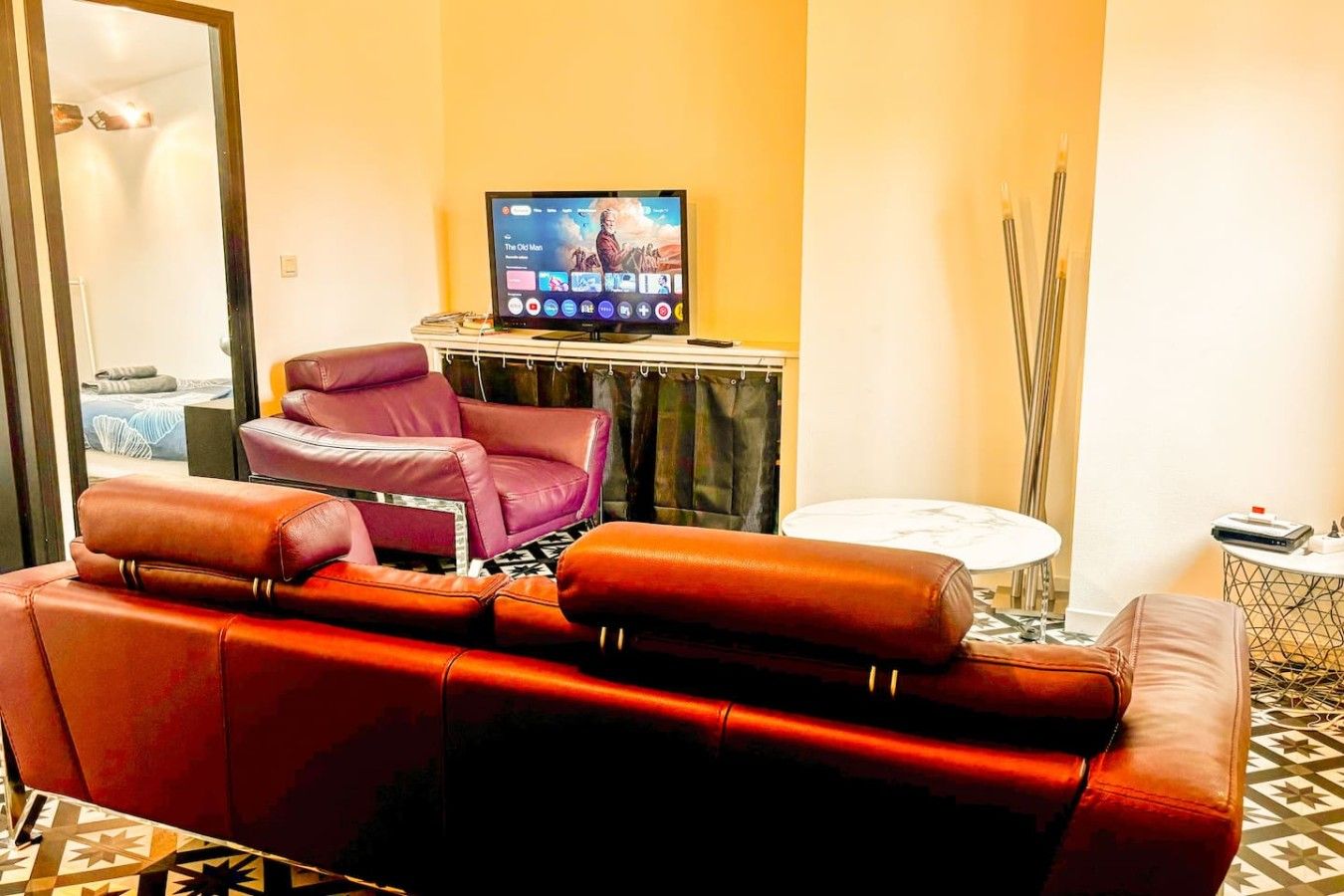 Een woonkamer met een rode leren bank, een paarse fauteuil, een televisie op een meubel en een kleine ronde tafel.
