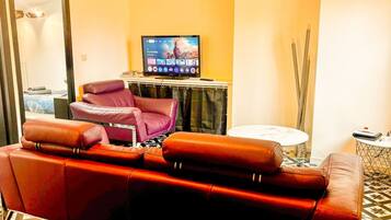 Een woonkamer met een rode leren bank, een paarse fauteuil, een televisie op een meubel en een kleine ronde tafel.
