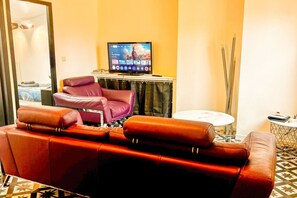 Ein Wohnzimmer mit einem roten Ledersofa, einem violetten Sessel, einem Fernseher auf einem Schrank und einem kleinen runden Tisch.
