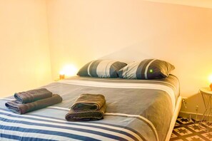 Ein ordentlich gemachtes Bett mit gestreifter Bettwäsche, zwei Kissen und zwei aufgerollten Handtüchern.