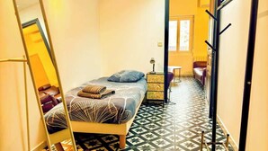 Una habitación de hotel estrecha con una cama, una mesita y una silla.