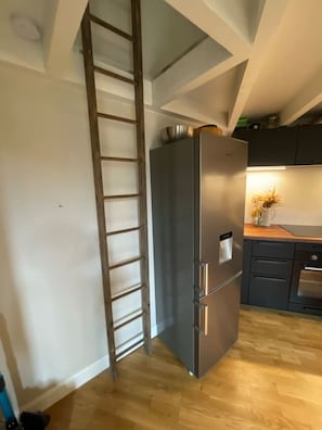 A kitchen with a stainless steel refrigerator, wooden flooring, and a wooden ladder against the wall. - Historic Bordeaux Loft: Charming Apartment in City (Bordeaux)