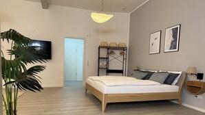 Ein modernes Schlafzimmer mit einem hölzernen Bett, einer Topfpflanze, einem Fernseher und einem Flur, der in einen anderen Raum führt.