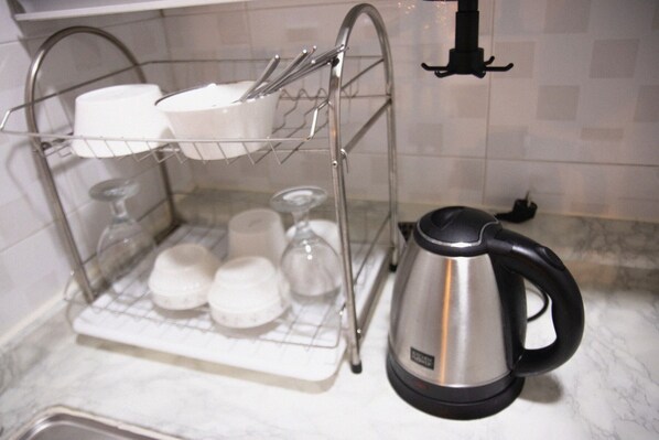 A kitchen with a dish rack holding bowls and glasses, a kettle, and a sink.