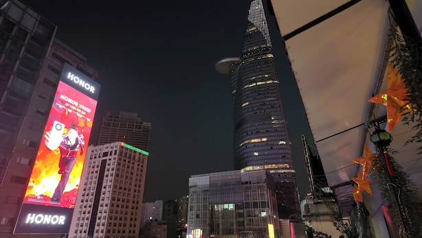 A cityscape with a prominent tower and a building with a large billboard advertising HONOR. - Prime Location 1BR – Nguyen Hue & Bitexco View (Thành phố Hồ Chí Minh)