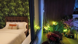 A bedroom with a bed, a window, and a view of a garden with plants and flowers. - Prime Location 1BR – Nguyen Hue & Bitexco View (Thành phố Hồ Chí Minh)