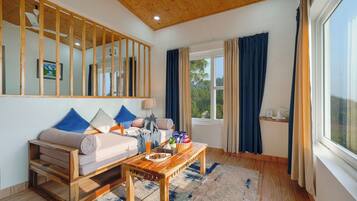 A cozy living room with a wooden ceiling, a sofa with cushions, a coffee table, and a large window with curtains.