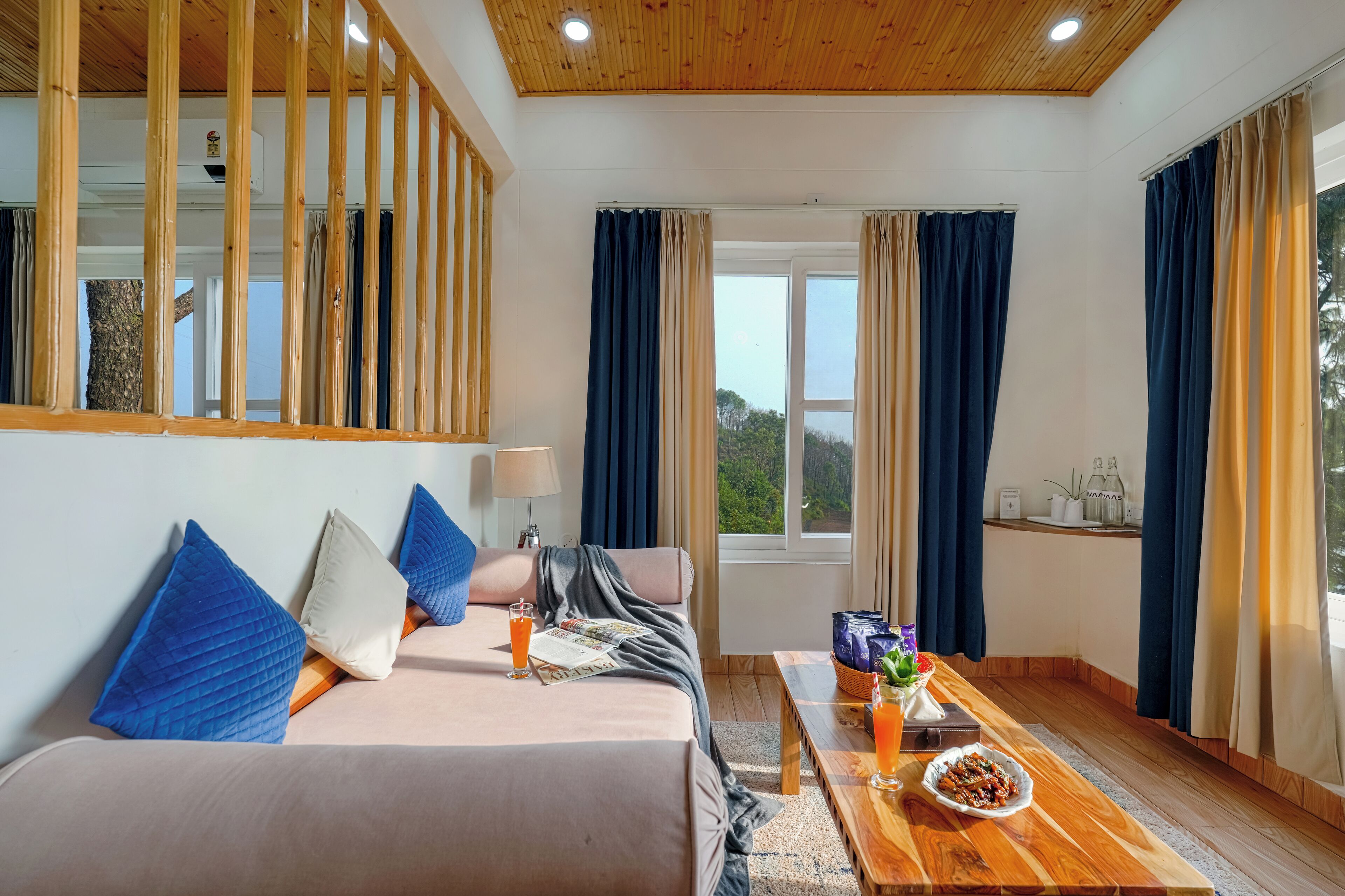 A modern room with a bed, a wooden coffee table, a window with curtains, and a view of greenery.