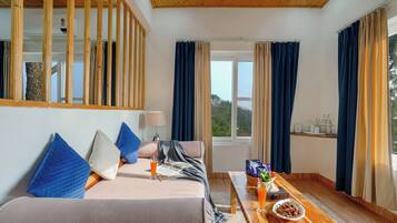 A modern room with a bed, a wooden coffee table, a window with curtains, and a view of greenery.