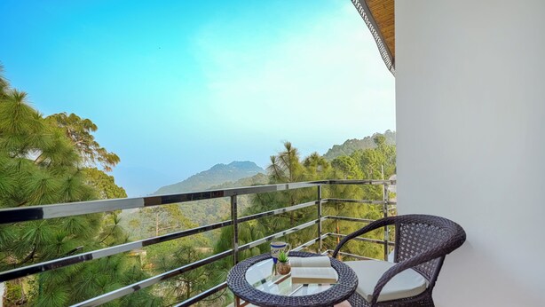 Een balkon met rieten stoelen en een tafel, met uitzicht op een weelderig groen landschap en verre bergen.