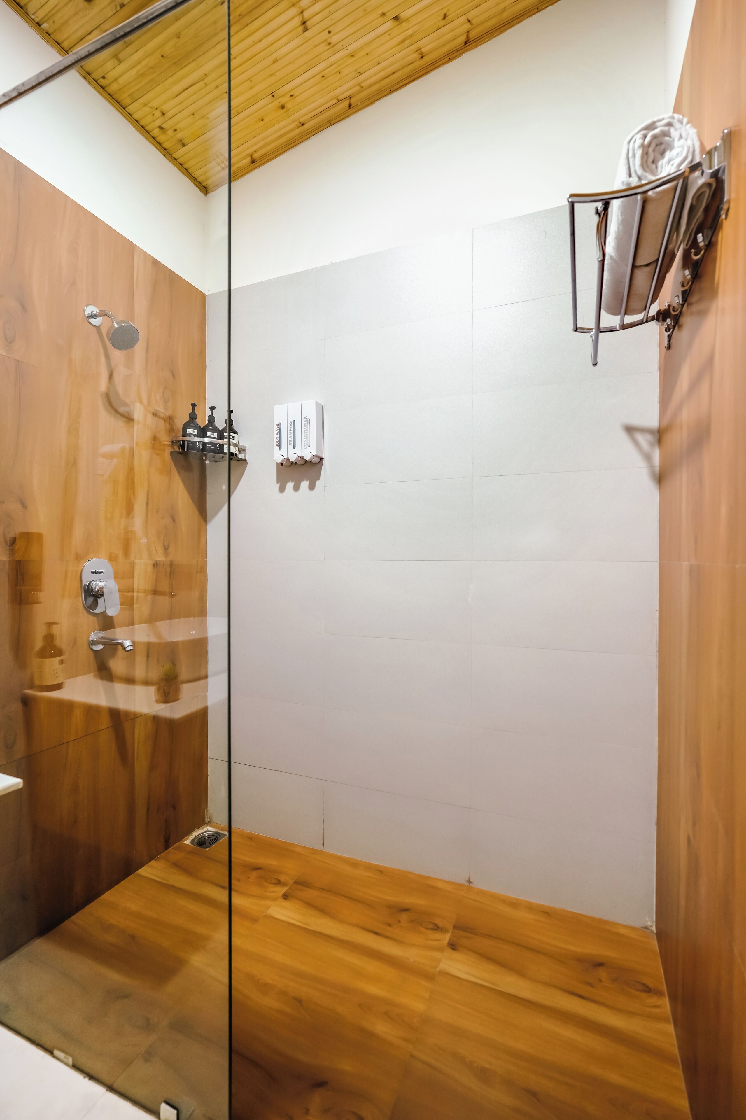 A modern bathroom with a glass shower enclosure, wooden flooring, and a towel rack on the wall.