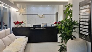 Een hotel receptie met een modern design, met een receptiebalie, een bank en een grote potplant.