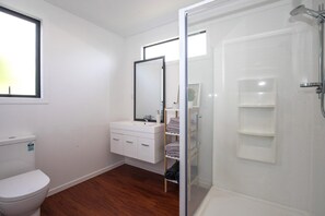 A bathroom with a toilet, a sink with a mirror, and a shower area. - Stay in Heaven at Lake Hawea (Lake Hāwea)