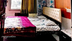A bedroom with a bed, a window with curtains, a ceiling fan, and a wall with a geometric pattern. - Shree krishna hotel  (Udaipur)