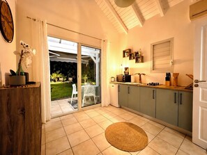 A kitchen with a sliding glass door leading to a patio, a coffee machine, and a small refrigerator. - Kaz A Doudou La – 2-bedroom apartment with terrace and garden, tropical calm (Saint-François)