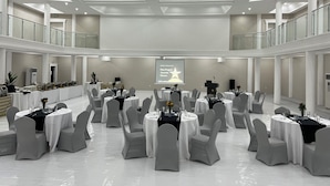 A spacious conference room with multiple round tables and chairs, a projector screen, and a balcony with glass railings. - Royal Ambassador Hotel (Harbel)