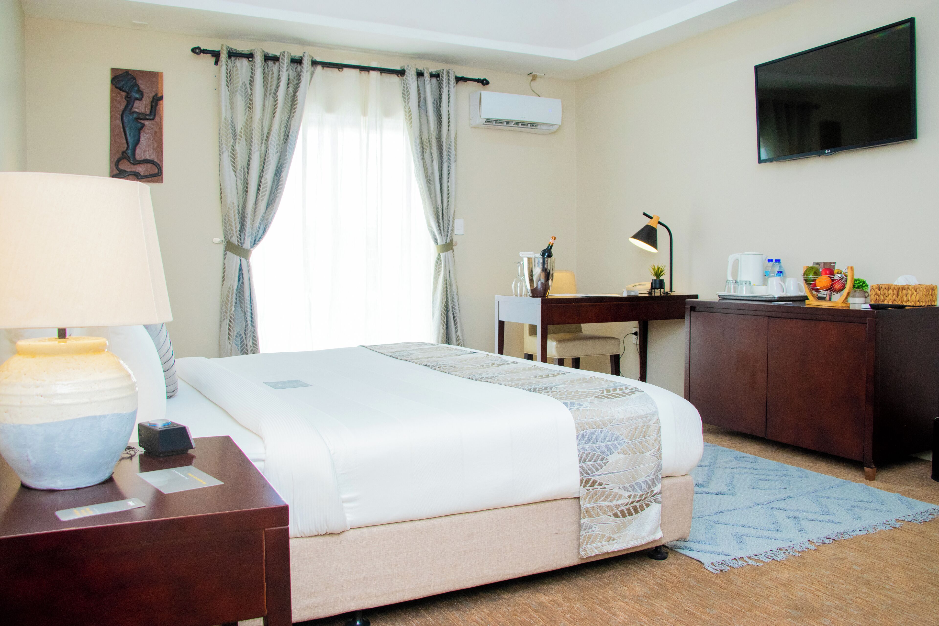 A hotel room with a bed, a desk, a chair, a TV, a lamp, a coffee maker, and a fruit basket.