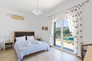 A bedroom with a bed, bedside tables, a ceiling fan, and a view of a pool and greenery. - Luxury seafront plot villa, seaviews, p-pool, walk to beach- Villa Alex Meganisi (Meganisi)