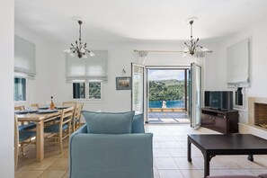 A modern living room with a sofa, dining table, and chairs, a TV, and a fireplace. - Luxury seafront plot villa, seaviews, p-pool, walk to beach- Villa Alex Meganisi (Meganisi)