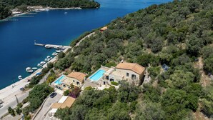 Uma propriedade costeira com piscina, um cais com barcos e vista para o mar e montanhas.