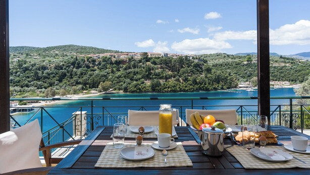 Mesa posta com itens de café da manhã e vista para um lago e colinas.