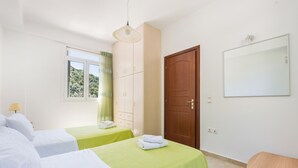 Quarto de hotel com duas camas, um guarda-roupa, um espelho e uma janela com vista para árvores.