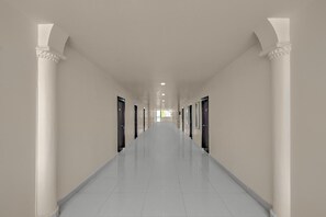 A long, narrow hallway with white walls and columns, leading to a bright end.