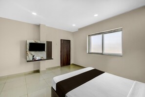 A hotel room with a bed, a TV mounted on the wall, a window, and a door. - Classic Hotel Lakshmi's Pride (Kurnool)