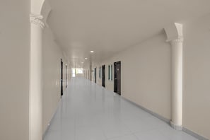 A long, narrow hallway with white walls and columns, leading to multiple doors. - Classic Hotel Lakshmi's Pride (Kurnool)