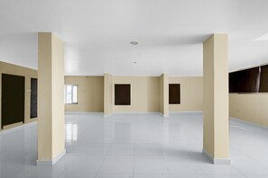 A spacious, empty room with white tiled floors and beige walls, featuring large windows and a flat ceiling. - Classic Hotel Lakshmi's Pride (Kurnool)