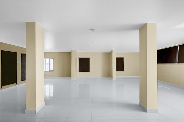 A spacious, empty room with white tiled floors and beige walls, featuring large windows and a flat ceiling.