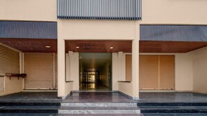 A building entrance with a set of marble steps leading up to a glass door, flanked by two closed shuttered doors.