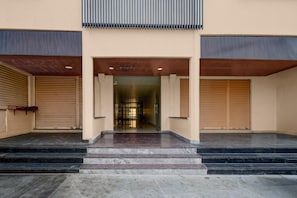 A building entrance with a set of marble steps leading up to a glass door, flanked by two closed shuttered doors.